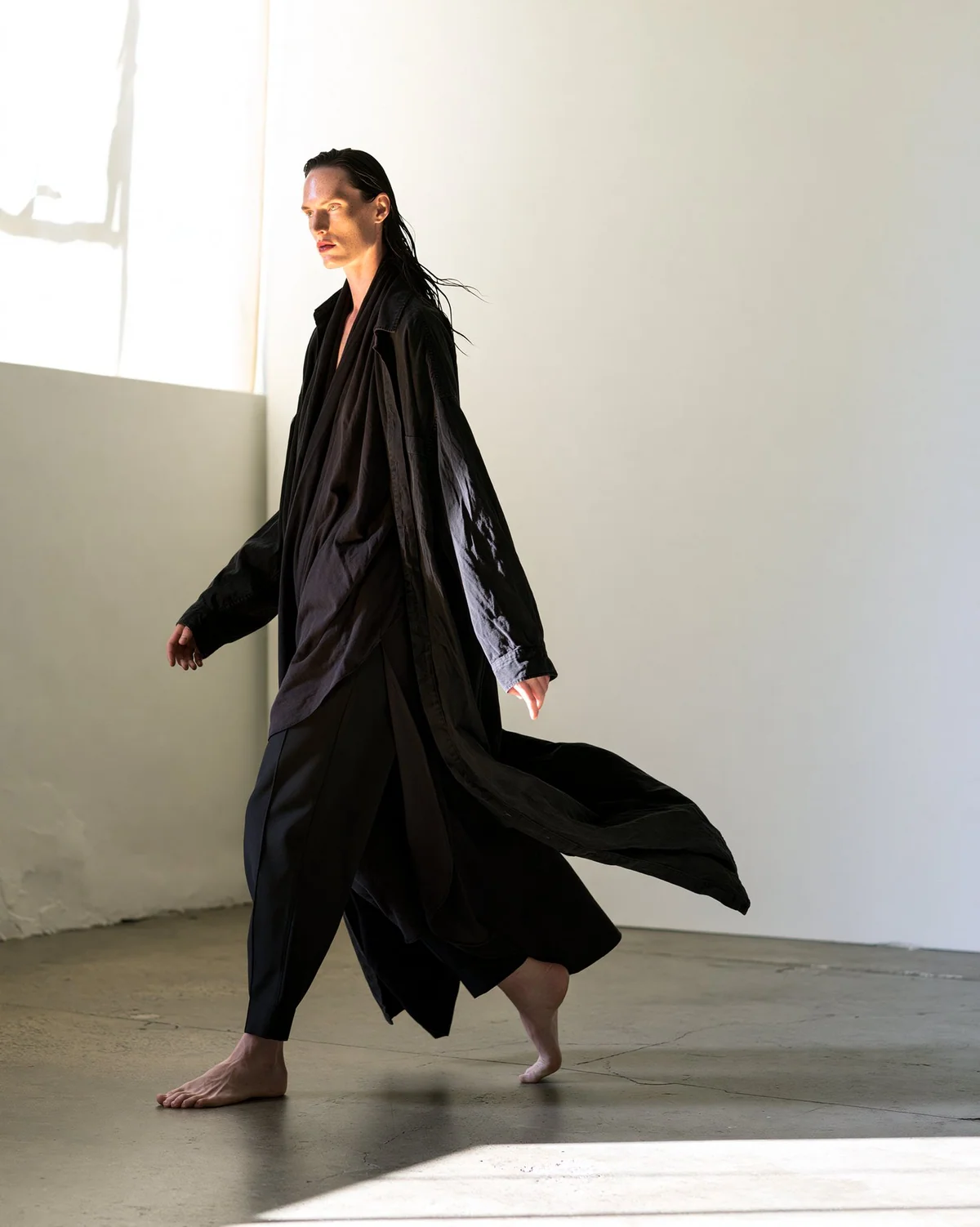 Full-body fashion model in black fabric captured in warm studio motion.