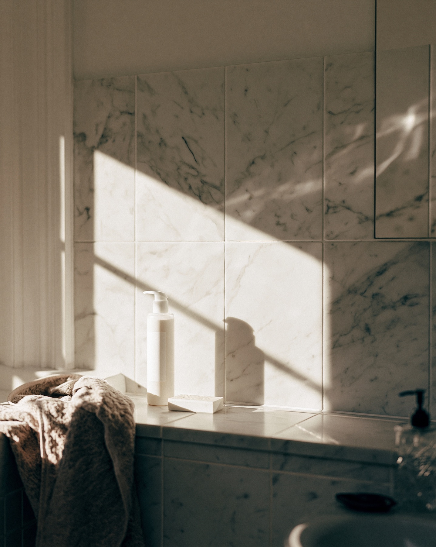 Minimal skincare products in a marble bathroom with long natural shadows.