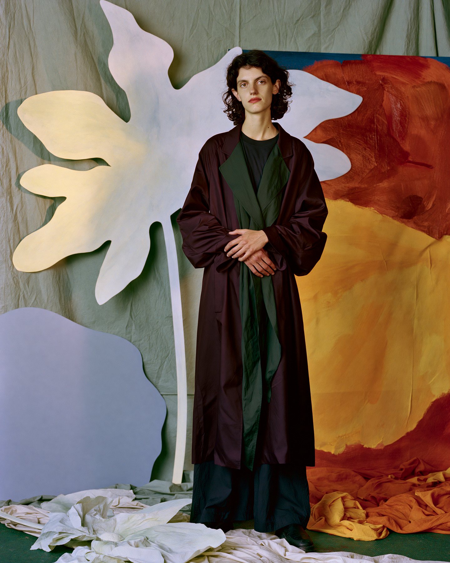Full-body fashion editorial model standing before a painterly studio wall.