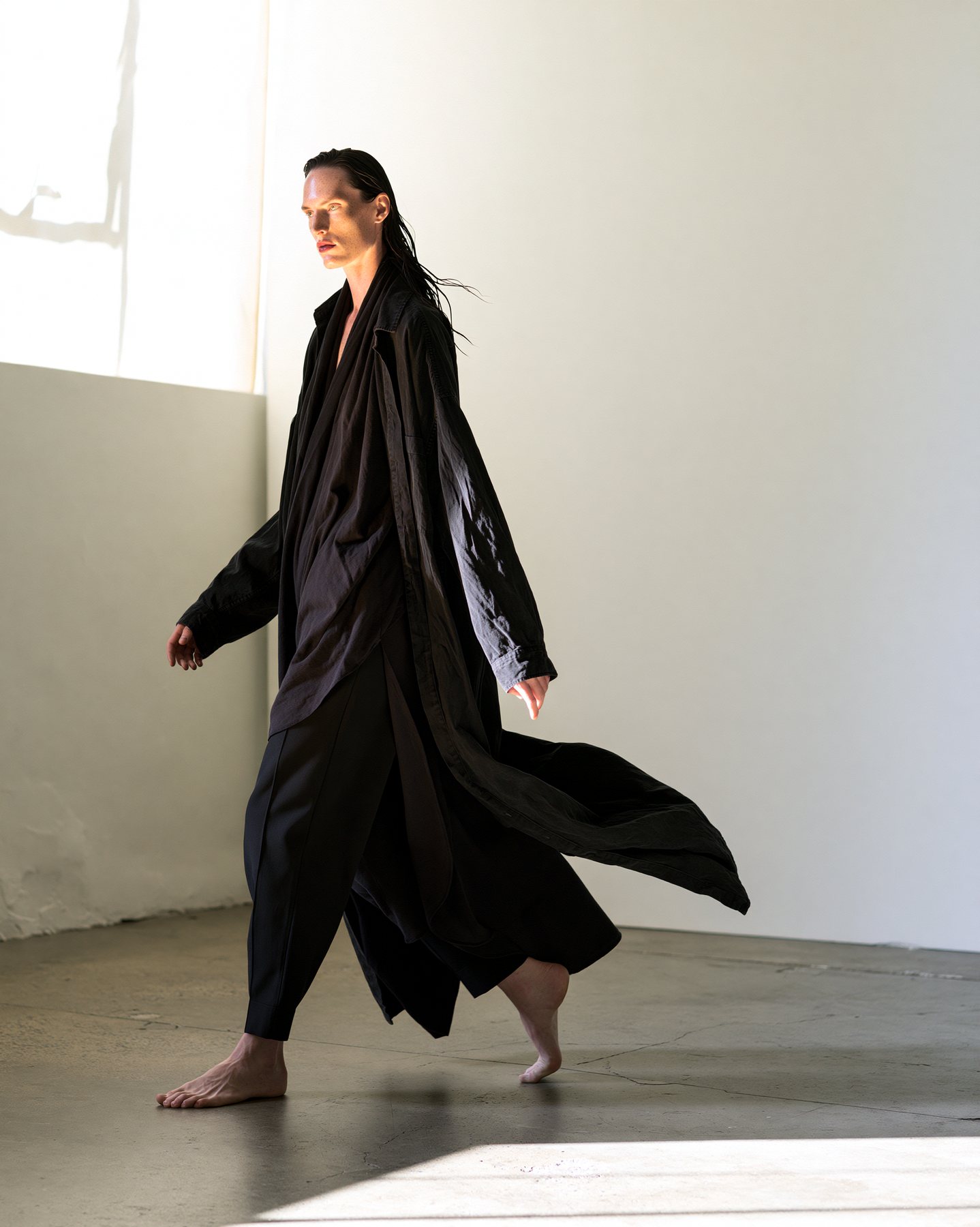 Full-body fashion model in black fabric captured in warm studio motion.