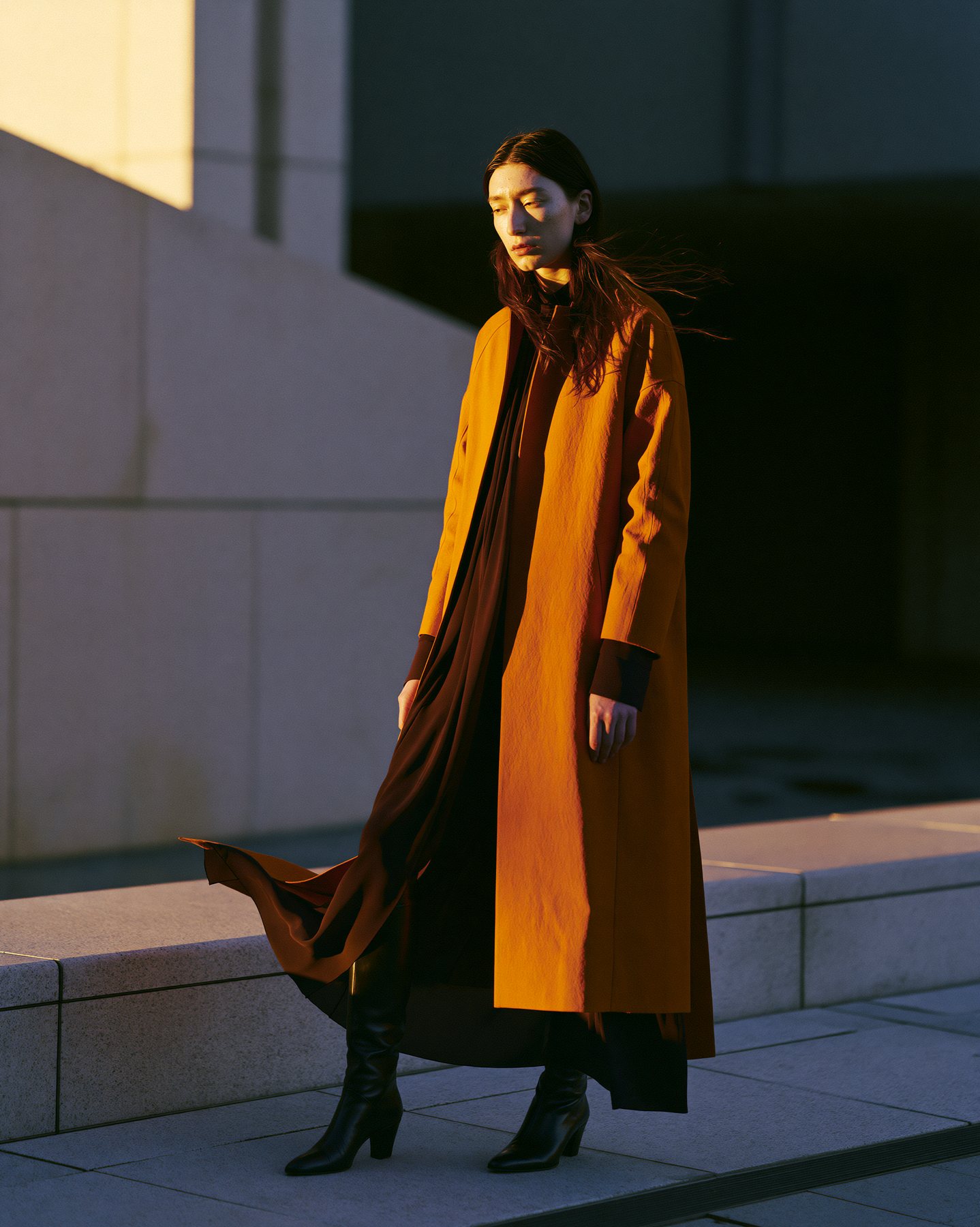 Dramatic full-body fashion editorial with amber coat and deep evening shadows.