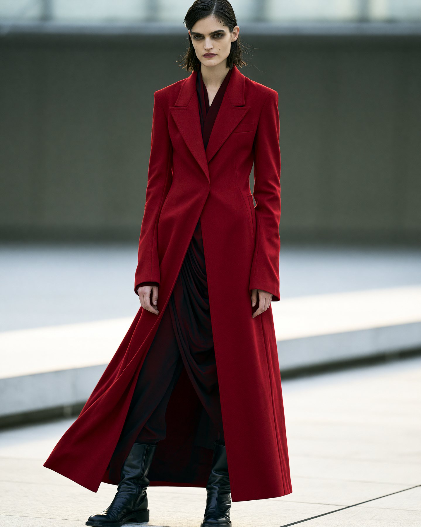 Full-body red coat fashion editorial photographed against a muted city backdrop.
