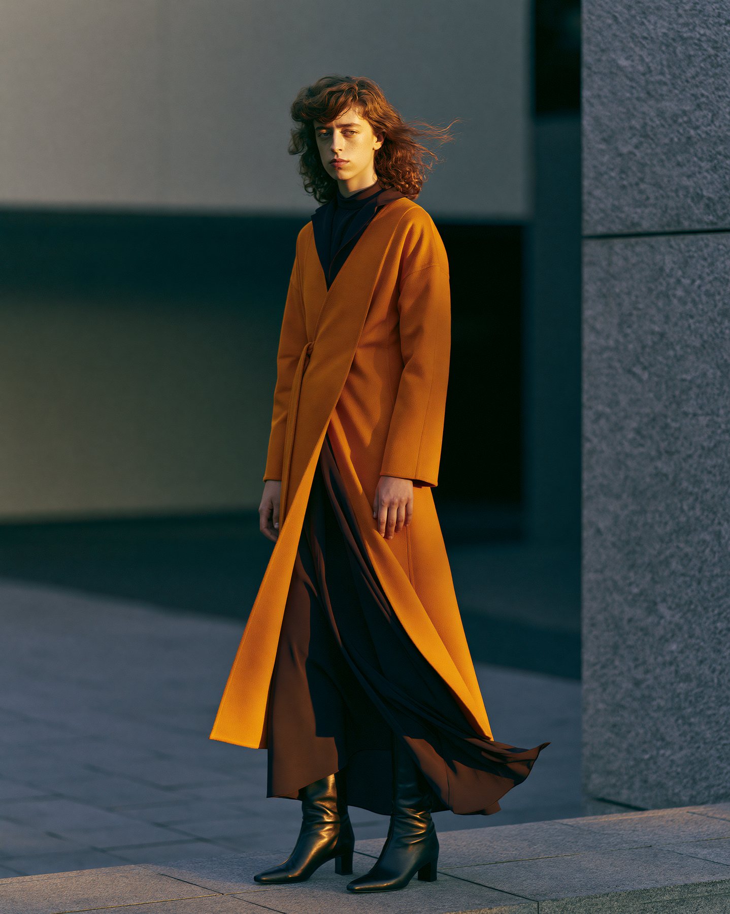 Full-body fashion editorial in an amber coat with sculptural evening light.