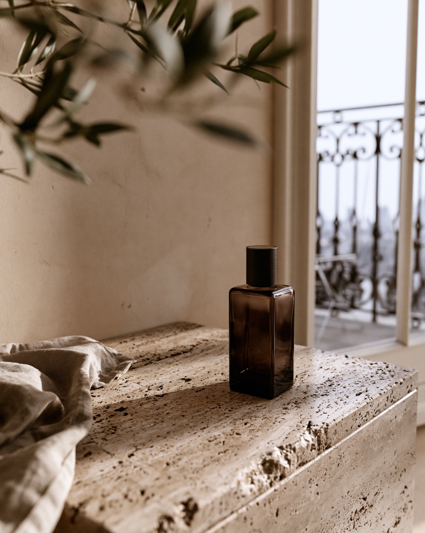 Dark unbranded fragrance bottle on travertine in soft balcony light.